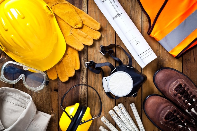 equipements-securite-btp-casque-gants-chantier-ocean.webp Équipements de sécurité pour le BTP : casque, gants, gilet fluorescent, chaussures et plans de chantier disposés sur une table en bois.