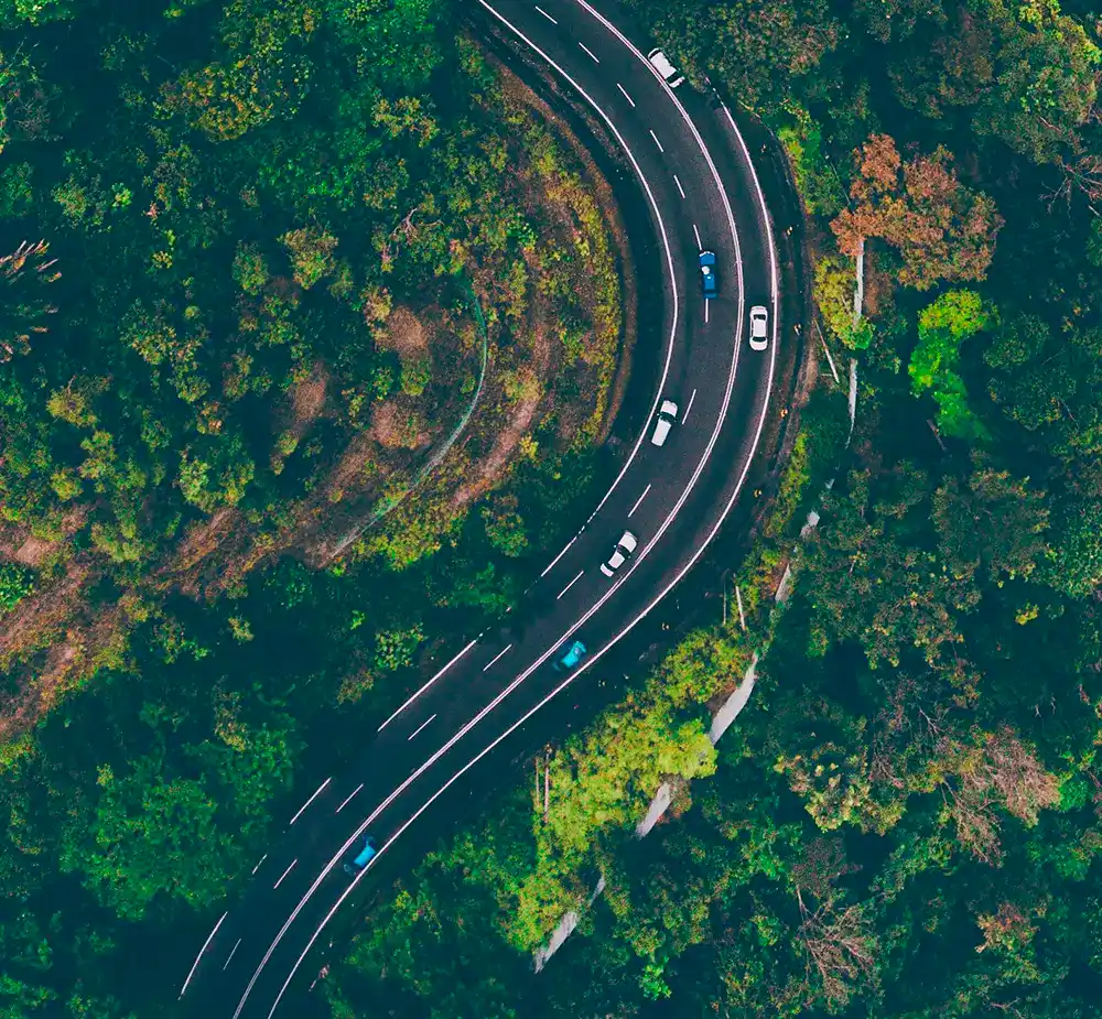 autopartage-reduction-couts-gestion-flotte-entreprise-ocean.jpg Vue aérienne d’une route sinueuse traversant une zone boisée, illustrant l’optimisation des déplacements professionnels et la réduction des coûts grâce à l’autopartage en entreprise.