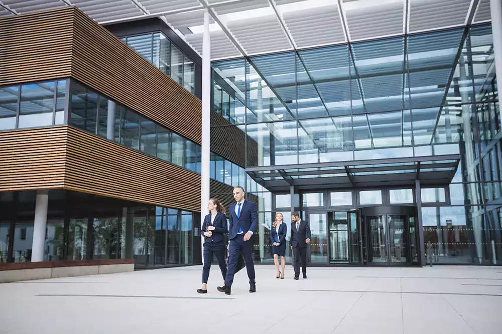 Employés quittant un immeuble de bureaux moderne, illustrant la gestion de flotte et la mobilité professionnelle en entreprise.